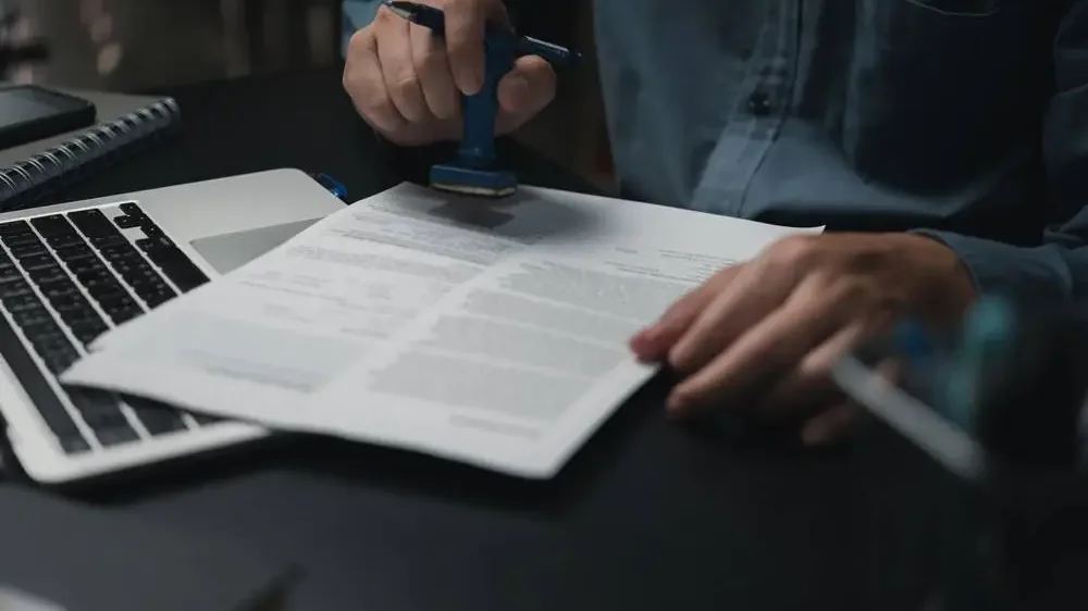 Traductor jurado sellando y firmando una traducción jurada urgente junto a un ordenador portátil